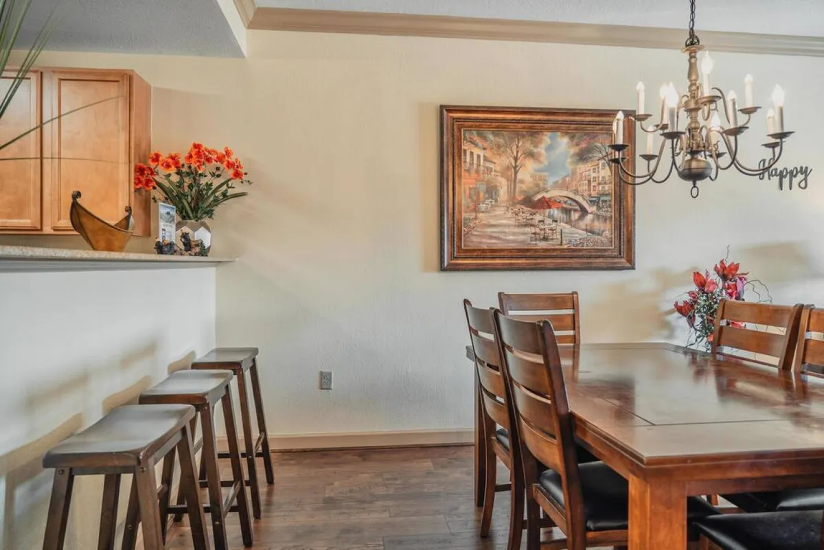 The dining area features a sturdy table with a beautiful flower arrangement, a glowing chandelier above, and thoughtful wall art creating a cozy backdrop. The space is inviting, perfect for shared meals or reconnecting over dinner.