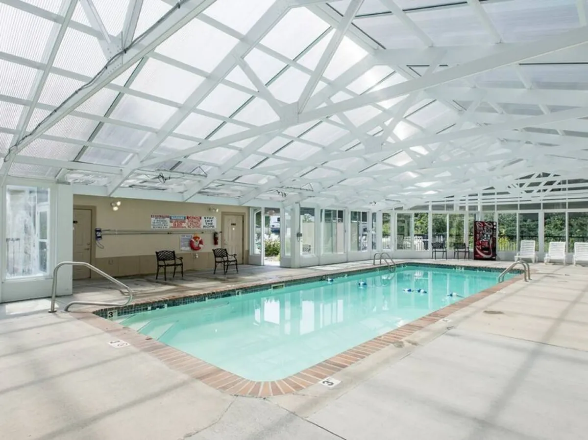 This image showcases the resort's indoor swimming pool, complete with a transparent roof that lets in natural light. Lounge chairs surround the pool, suggesting a space for guests to relax and unwind year-round, regardless of weather.
