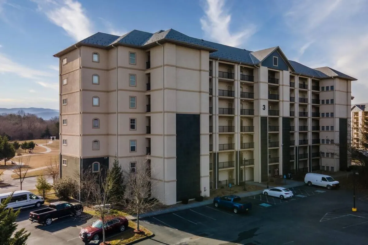 A multi-story building with ample parking, surrounded by green lawns and mature trees. The exterior offers a sense of community and accessibility, with balconies where guests can enjoy the fresh air and scenic surroundings.