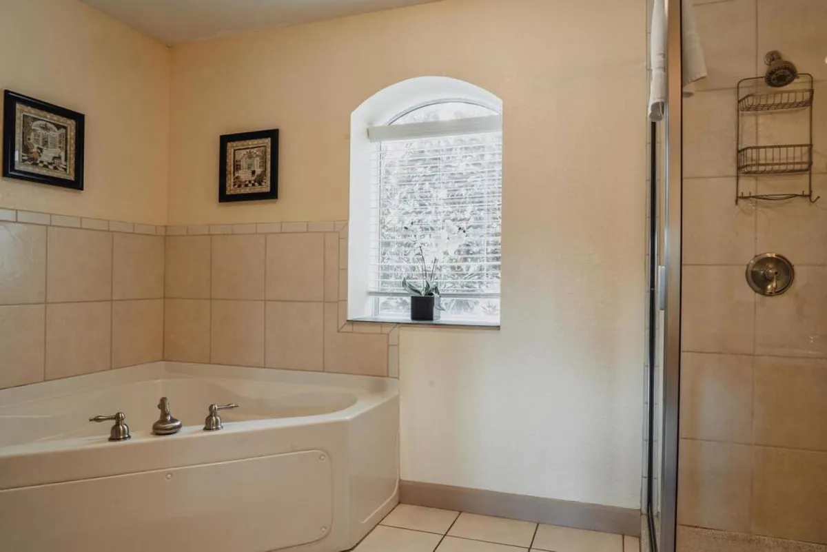 A tranquil bathroom setting featuring a jacuzzi (garden) tub, separate shower area, window with natural light, and decorative frames. The space feels open, airy, and spa-inspired, emphasizing relaxation and self-care.