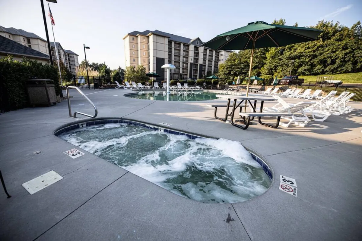 An outdoor scene featuring both a swimming pool and a hot tub, framed by lounge chairs, an umbrella, and a picnic table. The space looks inviting for both swimming and relaxed socializing, hinting at multi-generational enjoyment.