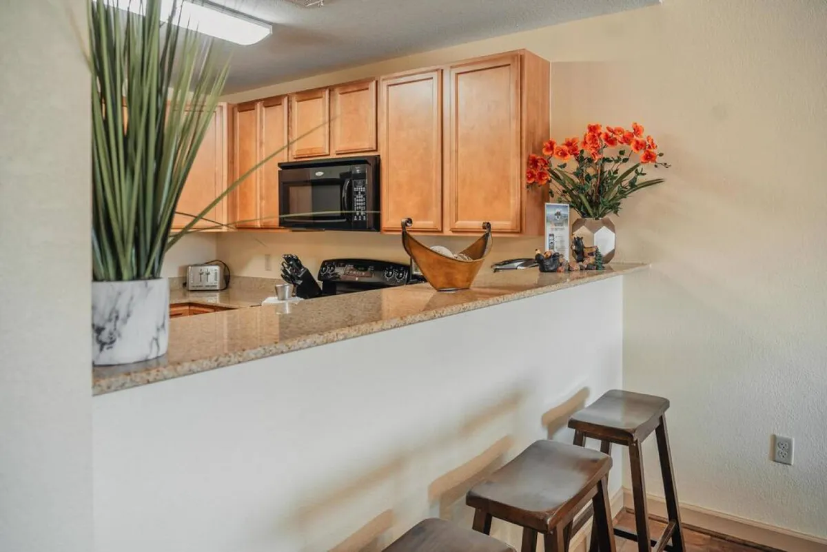 This image captures a spacious kitchen with stylish cabinetry, a central island adorned with decorative flowers, and bar stools inviting guests to gather. The open layout is ideal for group cooking sessions or casual breakfasts, reflecting a welcoming environment for culinary creativity.