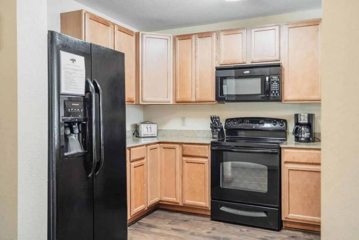 A warm and welcoming kitchen scene featuring black refrigerator and stove, a microwave, granite countertops, and ample wooden cabinetry. The generous workspace and modern appliances are well-suited for preparing group feasts or snacks before a day out.